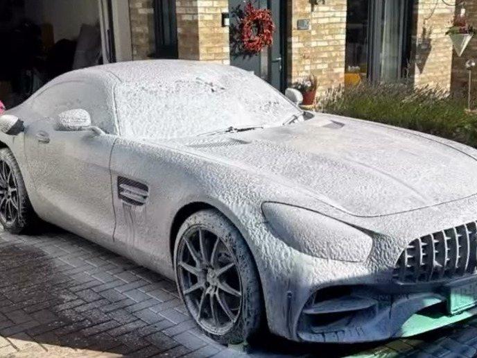 The same Mercedes‑AMG GT covered in snow foam mid-wash